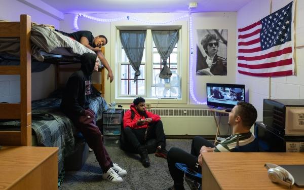 Male students in dorm room on bunkbeds watching tv and talking