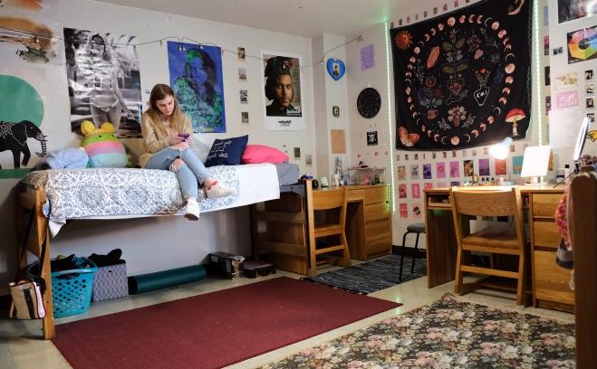 Female student sitting on bed in her dorm room looking at her phone