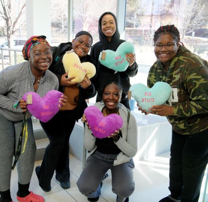 Female students showing off their stuffed heart pillows in Hammond street level